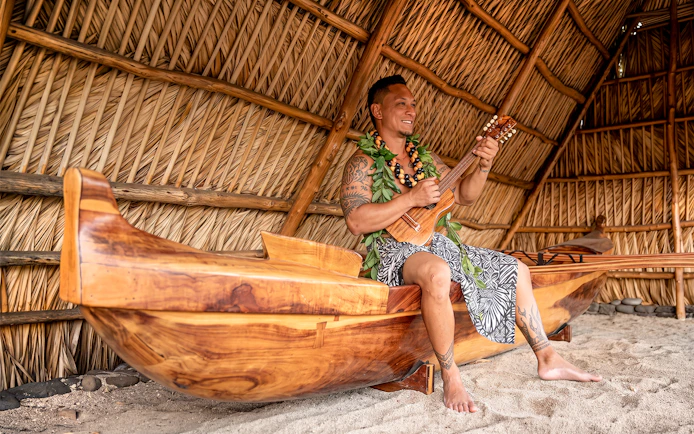 Man playing ukulele in traditional Hawaiian hut at Old Lahaina Luau.