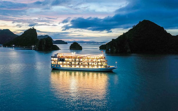 Cruise ship illuminated at night in Halong Bay with scenic islands in the background.