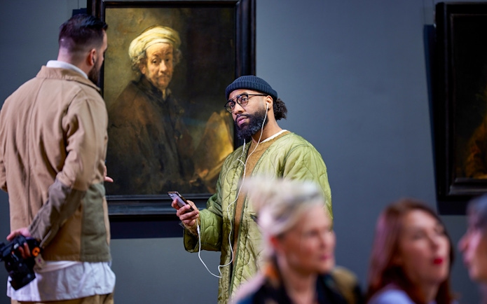 Visitors viewing Rembrandt's "Self-portrait as the Apostle Paul" at a museum exhibit.