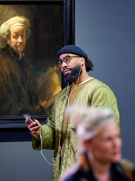 Visitors viewing Rembrandt's "Self-portrait as the Apostle Paul" at a museum exhibit.