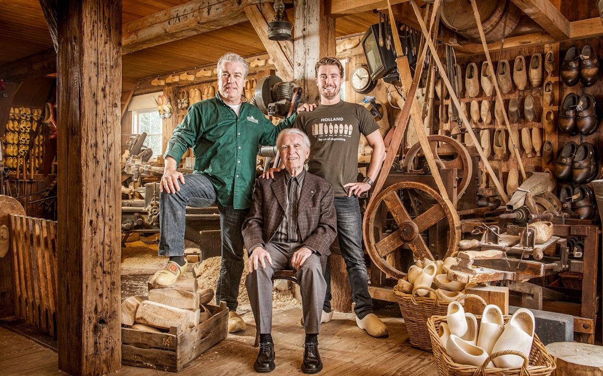 Artisans in a traditional Dutch workshop with wooden clogs and shoemaking tools.