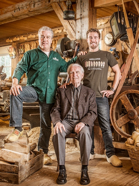 Artisans in a traditional Dutch workshop with wooden clogs and shoemaking tools.