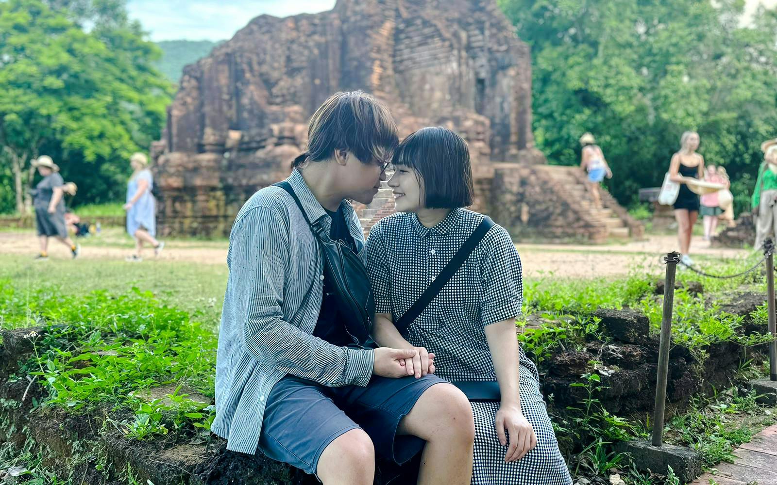 Couple sitting together at My Son Sanctuary, Vietnam, with ancient ruins in the background.
