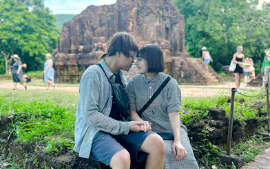 Couple sitting together at My Son Sanctuary, Vietnam, with ancient ruins in the background.