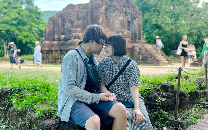 Couple sitting together at My Son Sanctuary, Vietnam, with ancient ruins in the background.