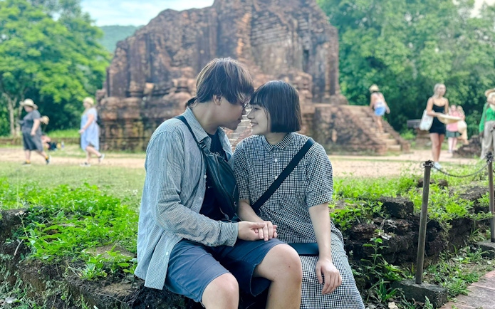 Couple sitting together at My Son Sanctuary, Vietnam, with ancient ruins in the background.