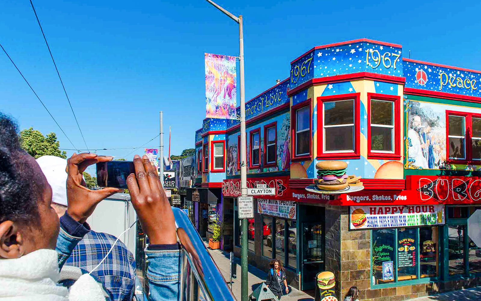 Tourists on a San Francisco hop-on hop-off bus photographing colorful Haight-Ashbury murals.