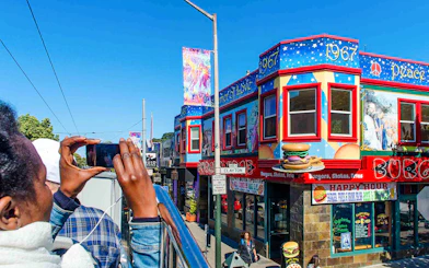 Tourists on a San Francisco hop-on hop-off bus photographing colorful Haight-Ashbury murals.