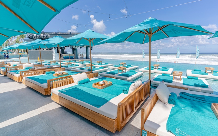 Poolside lounge beds at Atlas Beach Club overlooking the ocean, featuring turquoise umbrellas and towels.
