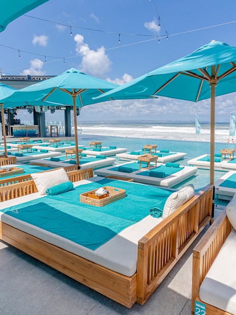 Poolside lounge beds at Atlas Beach Club overlooking the ocean, featuring turquoise umbrellas and towels.