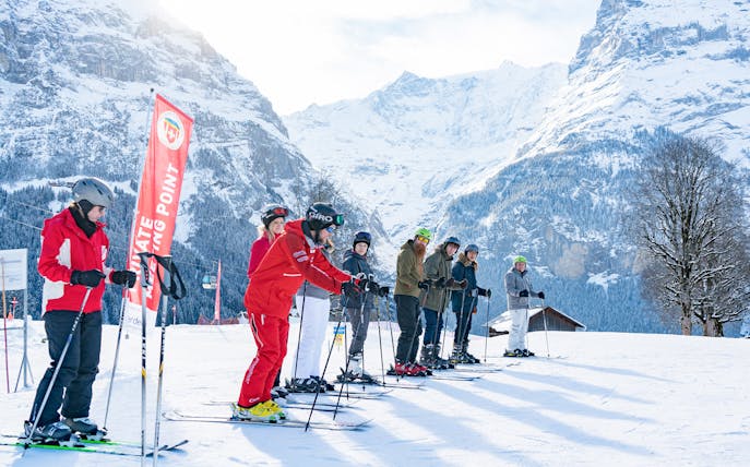 Group of skiers in Grindelwald with instructor, snowy mountains in background.