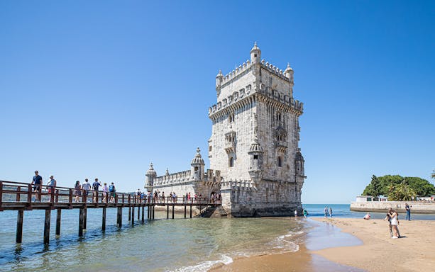 Belém Tower in Lisbon with tourists walking on a wooden bridge.