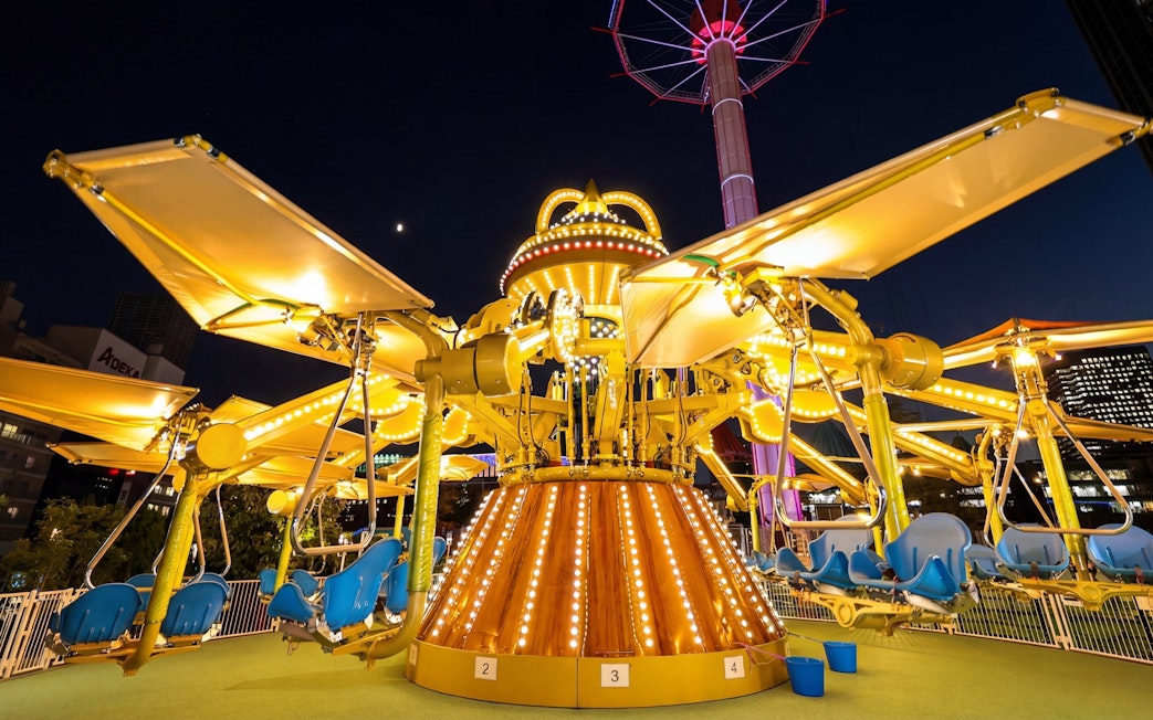 Amusement ride at night near Tokyo Dome with illuminated seats and structure.