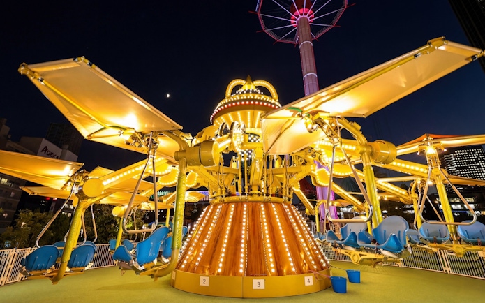 Amusement ride at night near Tokyo Dome with illuminated seats and structure.