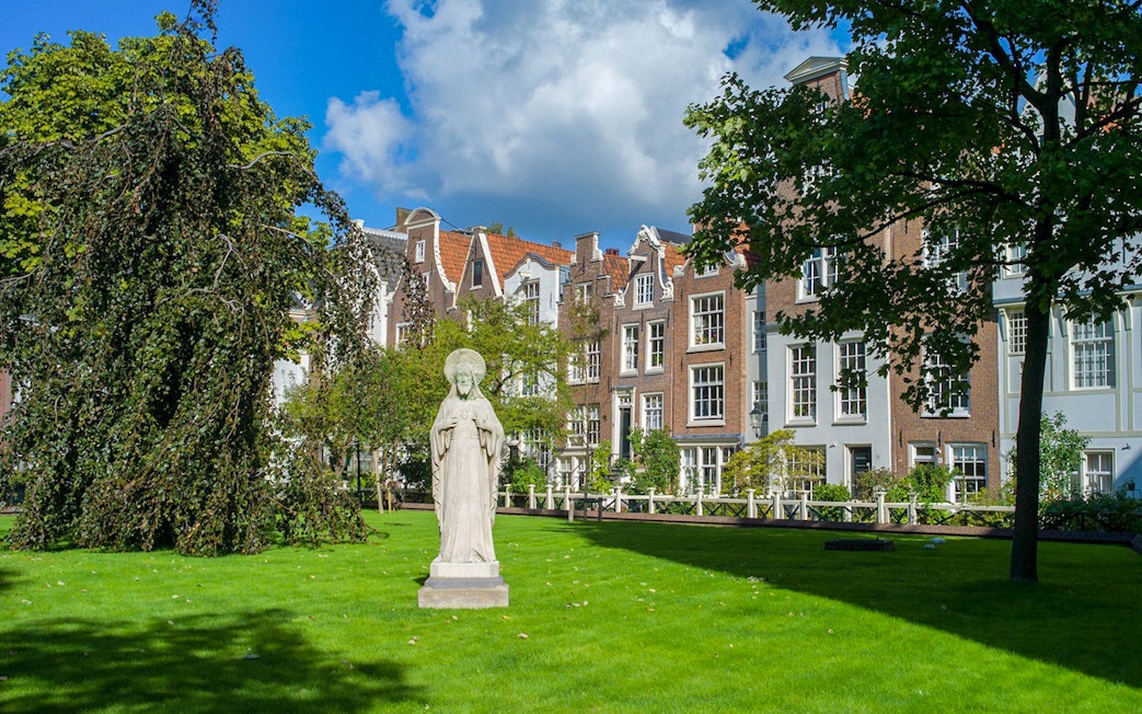 Statue in Begijnhof courtyard, Amsterdam, with historic buildings in the background.