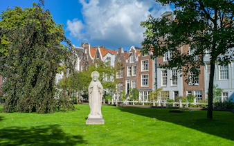 Statue in Begijnhof courtyard, Amsterdam, with historic buildings in the background.