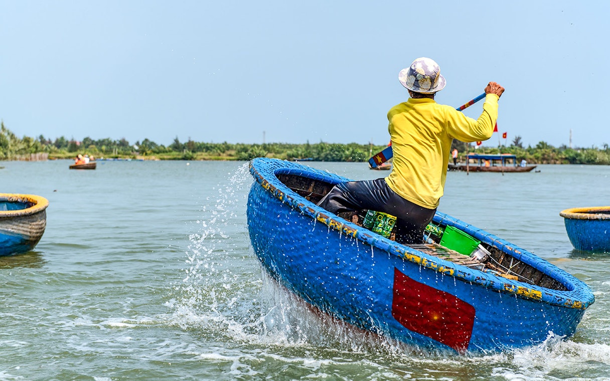 Person paddling a traditional blue bamboo basket boat in Vietnam.