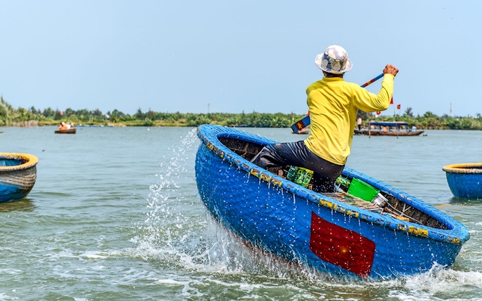 Person paddling a traditional blue bamboo basket boat in Vietnam.