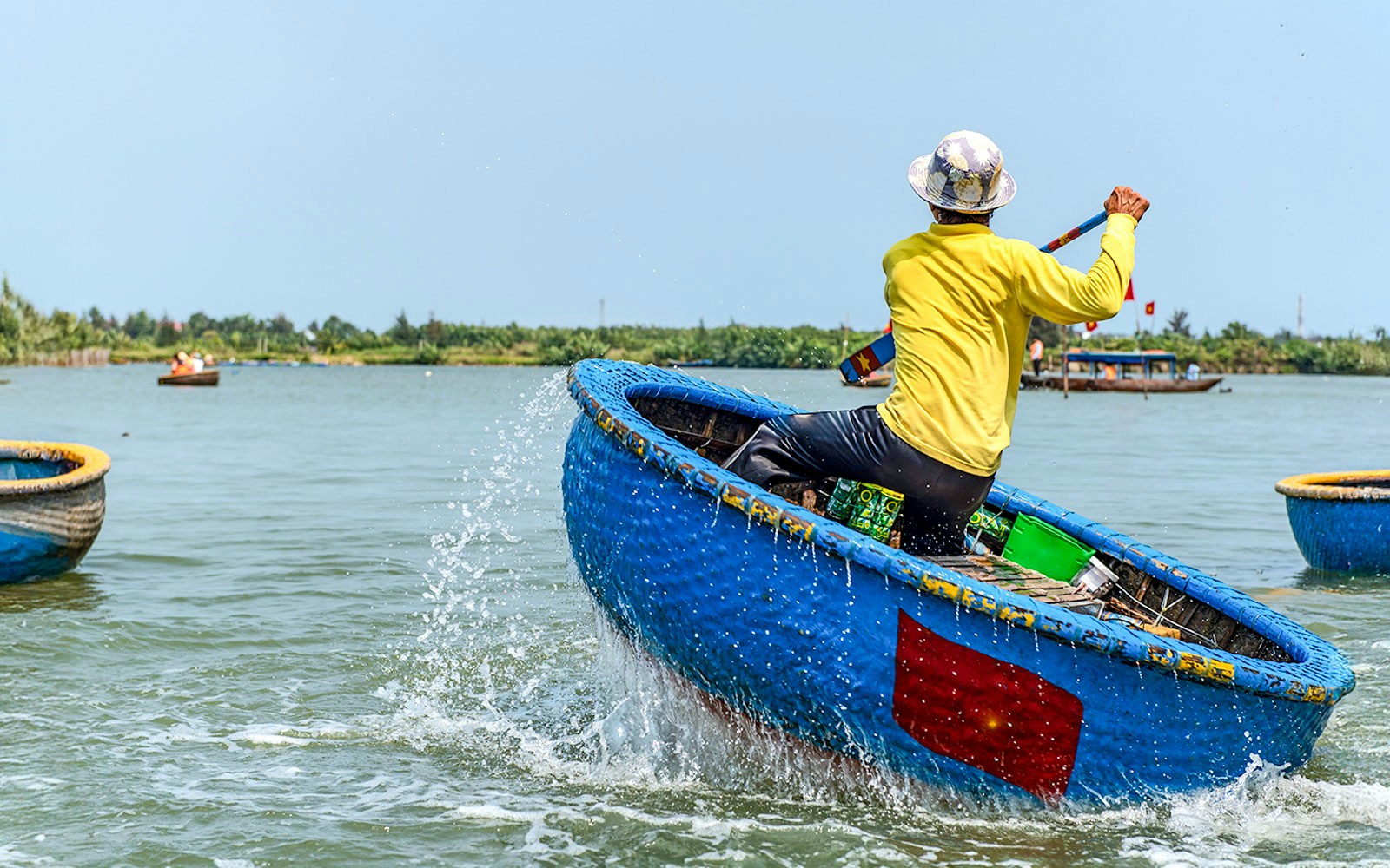 Person paddling a traditional blue bamboo basket boat in Vietnam.