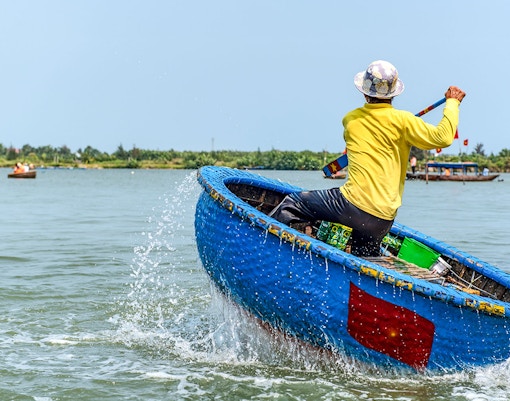 Person paddling a traditional blue bamboo basket boat in Vietnam.