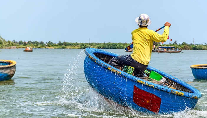 Person paddling a traditional blue bamboo basket boat in Vietnam.