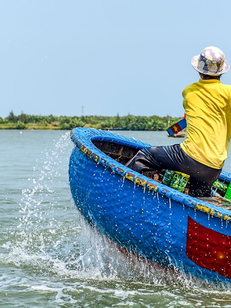 Person paddling a traditional blue bamboo basket boat in Vietnam.