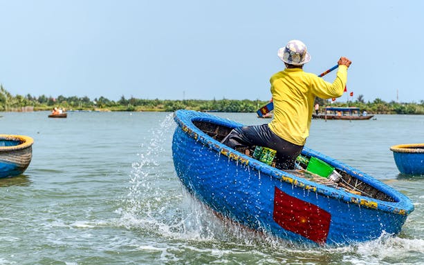 Person paddling a traditional blue bamboo basket boat in Vietnam.
