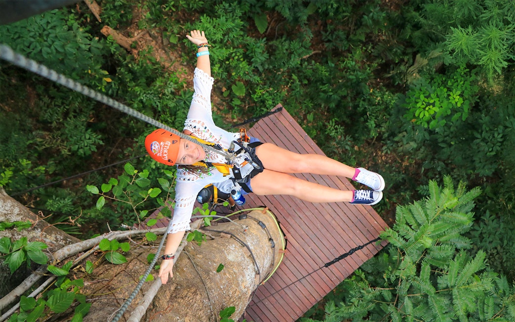 Lady ziplining at Hanuman World, Phuket, Thailand, surrounded by lush forest.