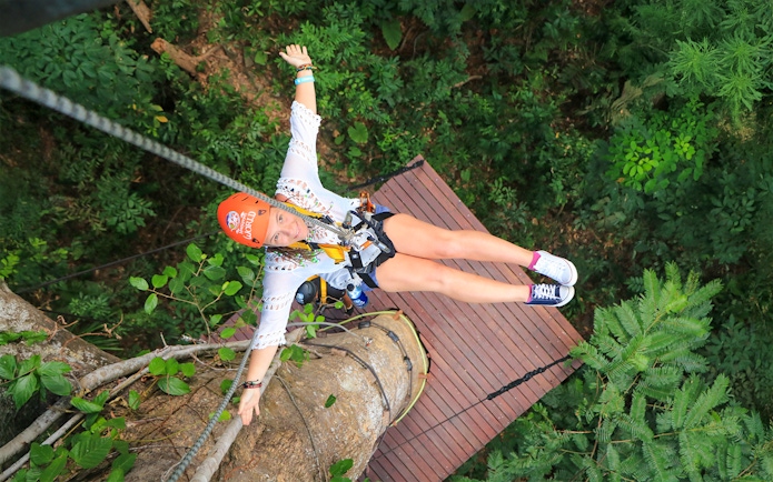 Lady ziplining at Hanuman World, Phuket, Thailand, surrounded by lush forest.