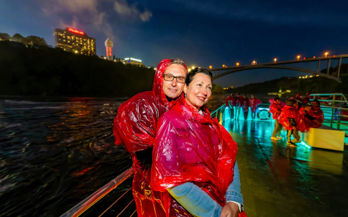 Couple in red ponchos on Niagara Falls fireworks boat cruise at night.
