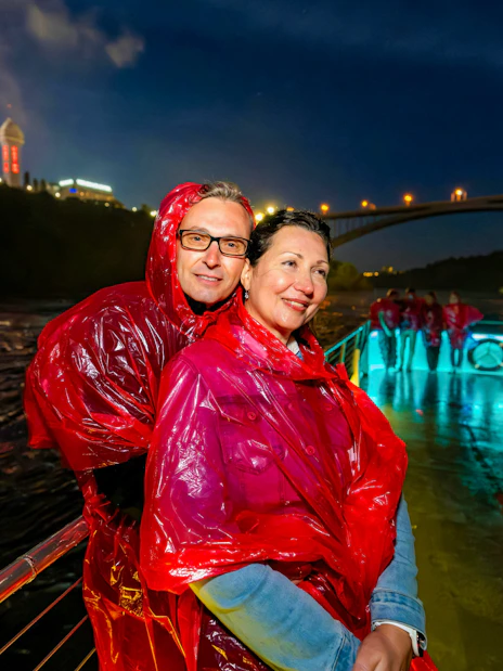 Couple in red ponchos on Niagara Falls fireworks boat cruise at night.