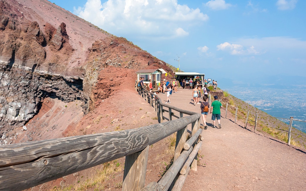 Visitors walking along the path on Mount Vesuvius with a view of the crater and Naples in the distance.