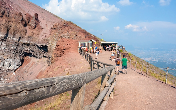 Visitors walking along the path on Mount Vesuvius with a view of the crater and Naples in the distance.