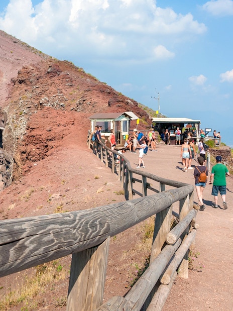 Visitors walking along the path on Mount Vesuvius with a view of the crater and Naples in the distance.