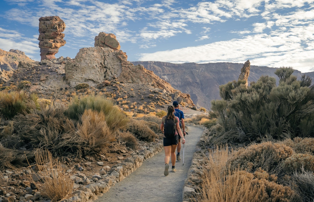 Hikers with backpacks on a trail in Teide National Park, near Roques de García's volcanic rocks.
