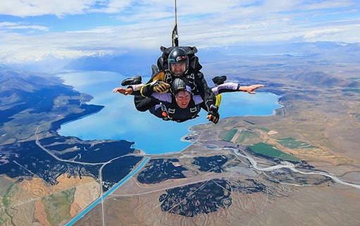 Skydivers tandem jumping over Lake Pukaki with Mt Cook in the background, New Zealand.