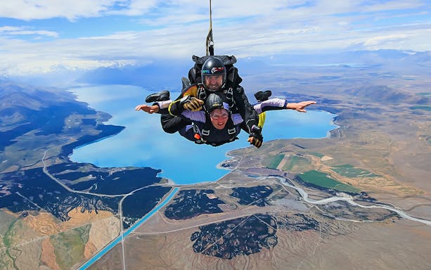Skydivers tandem jumping over Lake Pukaki with Mt Cook in the background, New Zealand.
