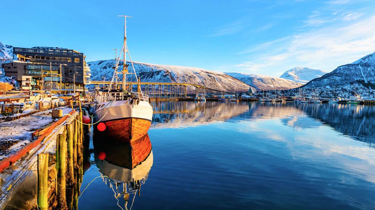 RIB boat docked in Tromso harbor with snowy mountains in the background, Norway.