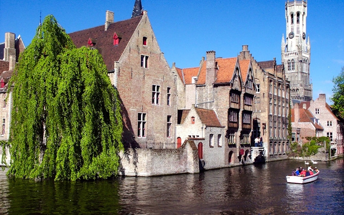 Boat tour on the canals of Brugge with historic buildings and Belfry tower in view.