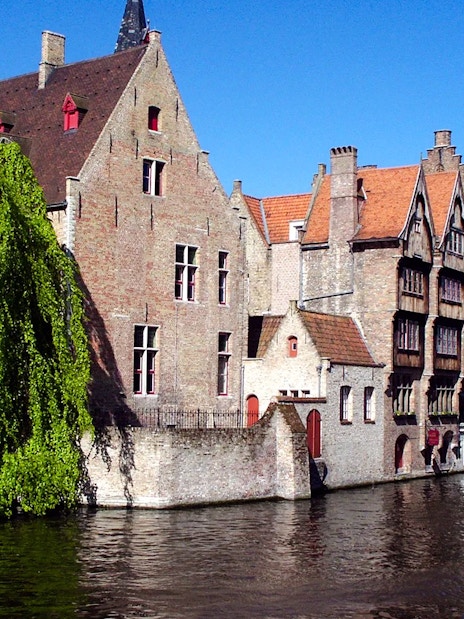 Boat tour on the canals of Brugge with historic buildings and Belfry tower in view.