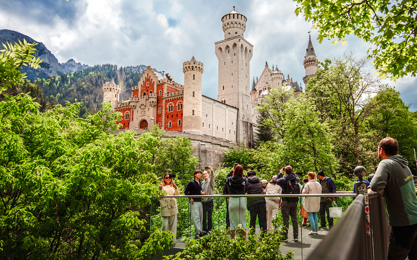 Tourists on a bridge with Neuschwanstein Castle in the background, Bavaria, Germany.