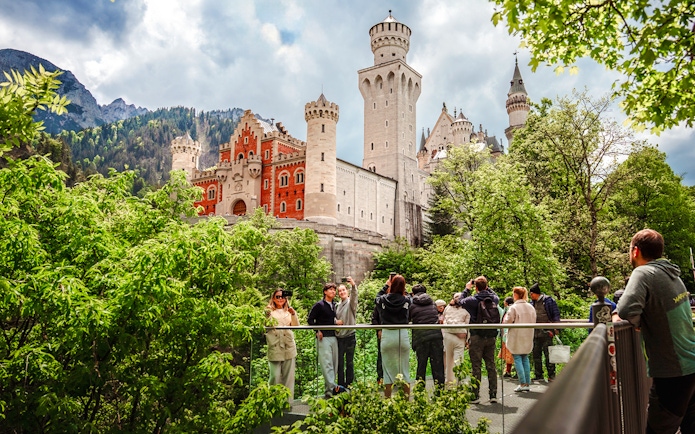 Tourists on a bridge with Neuschwanstein Castle in the background, Bavaria, Germany.
