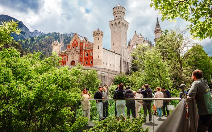 Tourists on a bridge with Neuschwanstein Castle in the background, Bavaria, Germany.