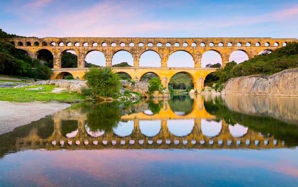 Pont du Gard aqueduct reflecting in the Gardon River, France, with surrounding greenery.