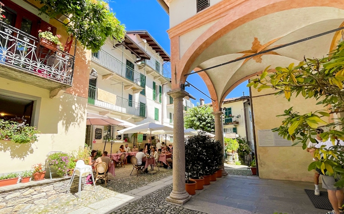 Outdoor café scene on Isole Borromee with people dining under umbrellas, surrounded by historic architecture.