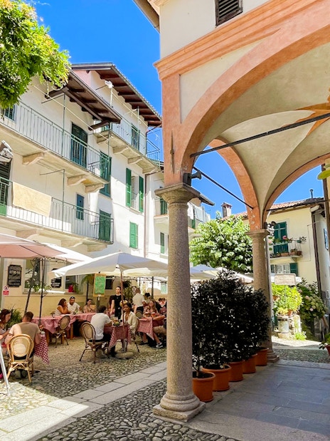 Outdoor café scene on Isole Borromee with people dining under umbrellas, surrounded by historic architecture.