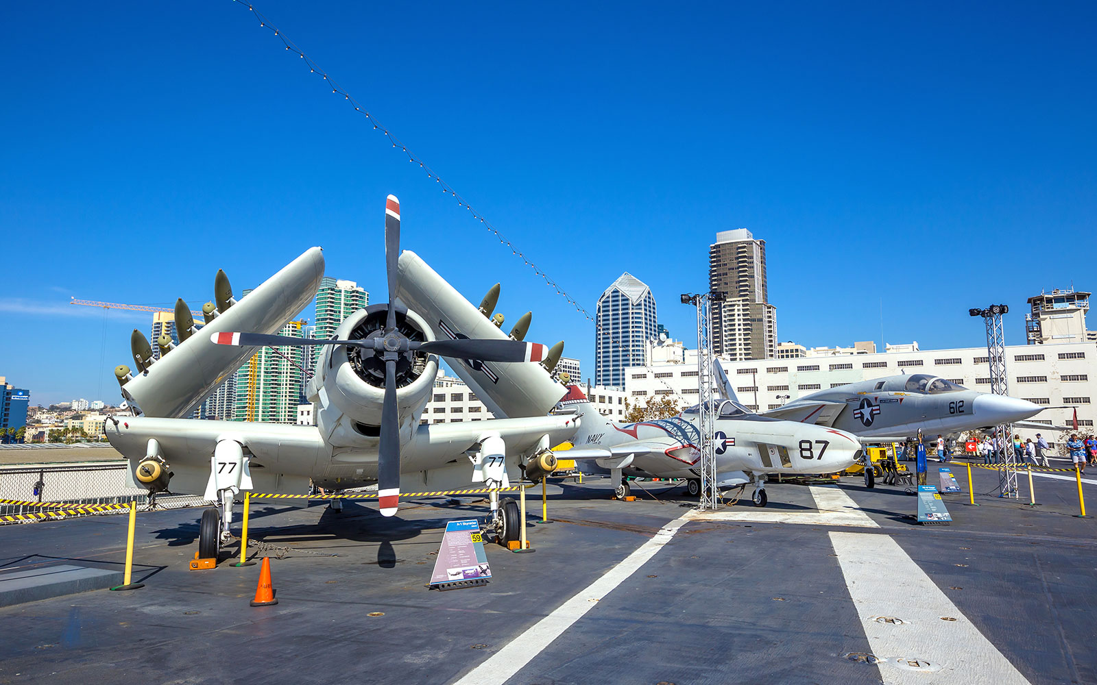 Aircraft display on USS Midway Museum deck, San Diego skyline in background.