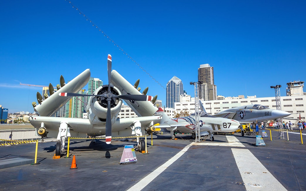 Aircraft display on USS Midway Museum deck, San Diego skyline in background.