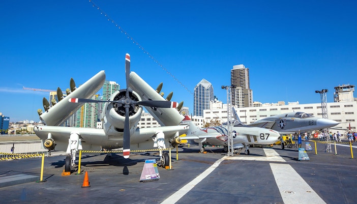 Aircraft display on USS Midway Museum deck, San Diego skyline in background.