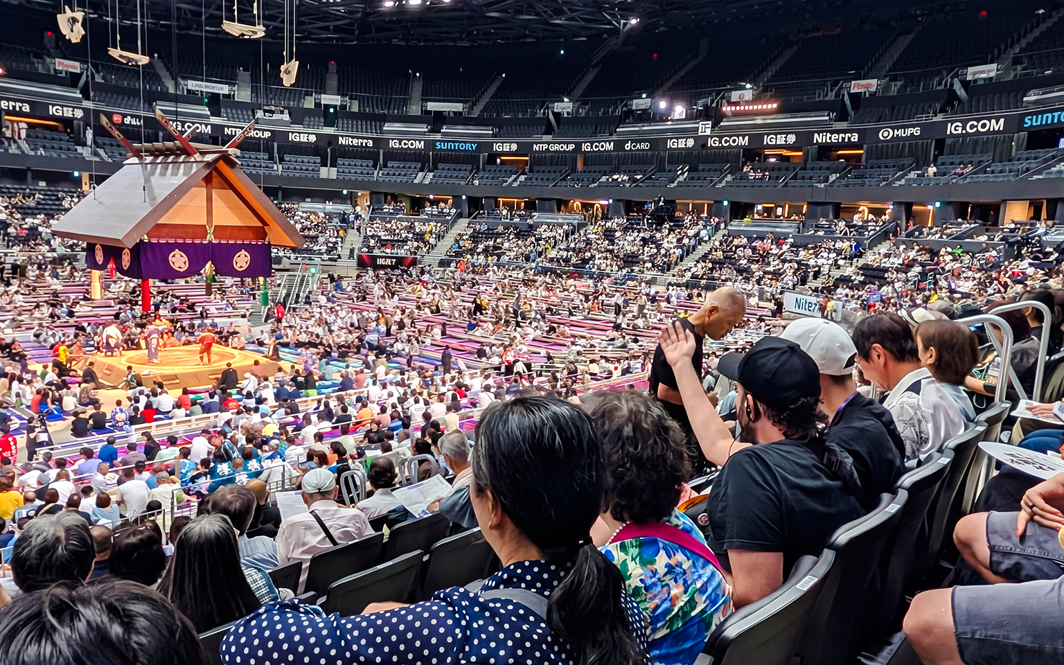 Spectators watching a sumo match at the Nagoya Grand Sumo Tournament in a crowded arena.